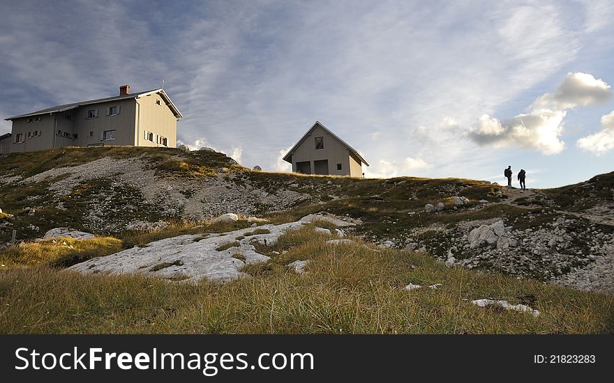 Alpine lodge in the middle of Slovenian Alps - scenery with sunset and two hikers at Pogacnikov dom