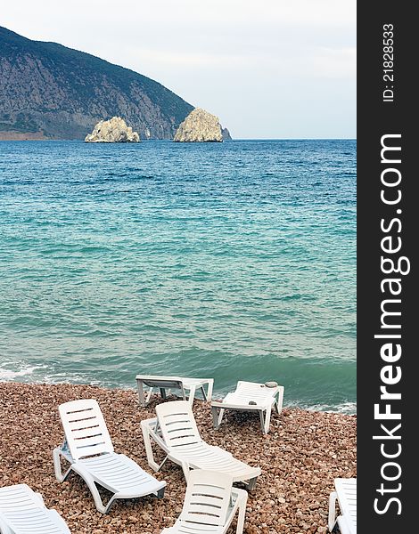 Several empty lounges on the beach, blue sea, two rocks, mountain. Season closed. Several empty lounges on the beach, blue sea, two rocks, mountain. Season closed.