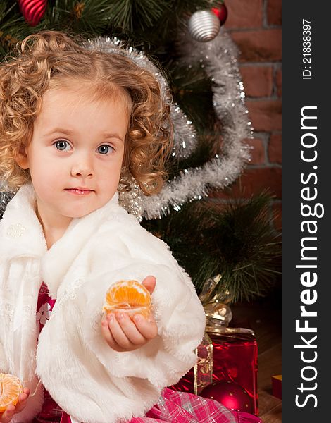 Preaty little girl eating tangerine near Christmas tree