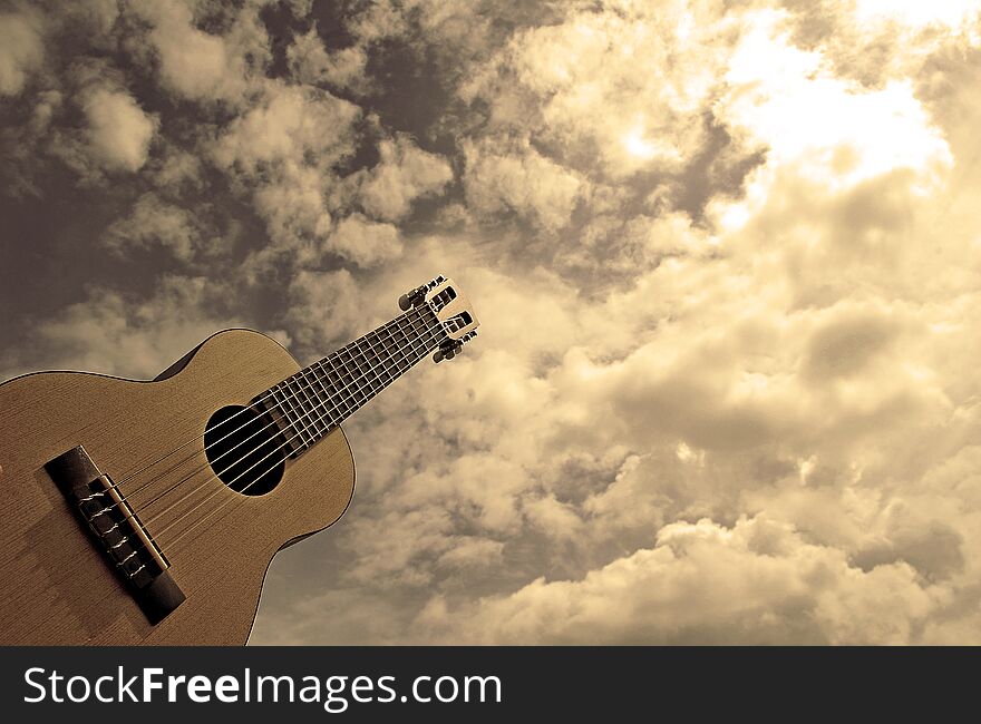 Color photography of guitalele music instrument, little guitar or guitar-ukulele hybrid with gray sky in the background. Color photography of guitalele music instrument, little guitar or guitar-ukulele hybrid with gray sky in the background