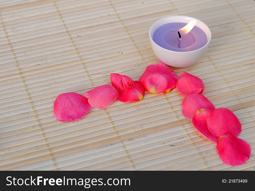 Purple candle with rose petals on bamboo