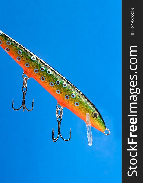 A fishing bait (wobbler) with hooks on a blue background. A fishing bait (wobbler) with hooks on a blue background