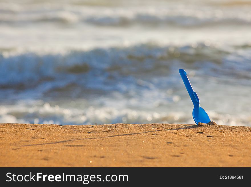 Blue shovel in the yellow sand near sea