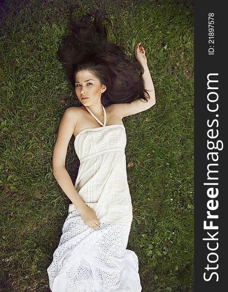 A girl with long dark hair wearing a white dress lying on grass. A girl with long dark hair wearing a white dress lying on grass