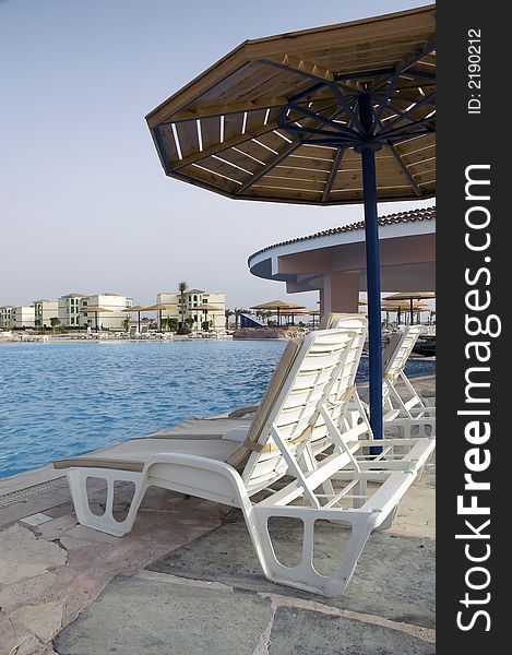 Overview at resort pool at a sunrise with chairs and umbrella at front. Overview at resort pool at a sunrise with chairs and umbrella at front