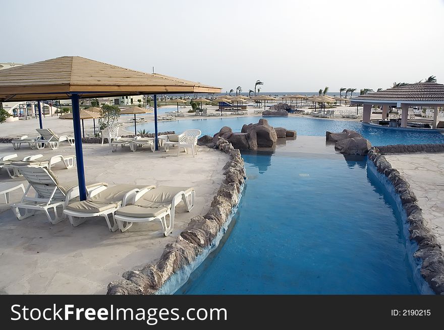 Overview at wide angle at the resort pool system with sunshades and chairs at sunrise. Overview at wide angle at the resort pool system with sunshades and chairs at sunrise