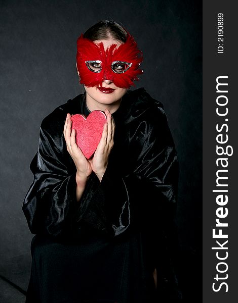 Women in red mask with heart-box in hands. Make-up black background. Women in red mask with heart-box in hands. Make-up black background.