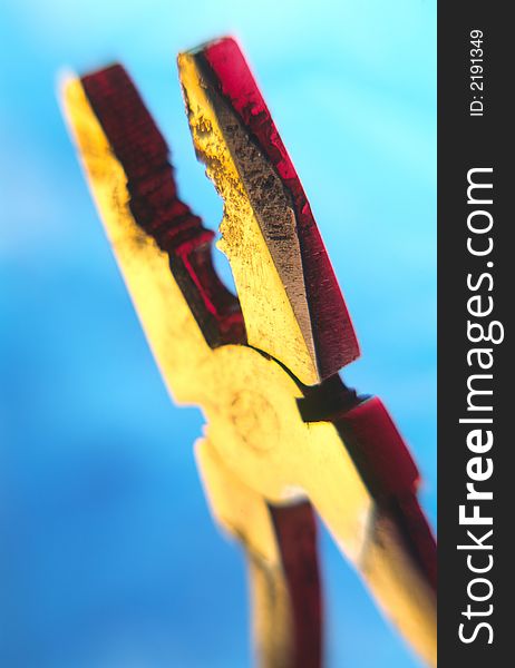 Old flat-nose pliers covered by light on  blue background,  close up