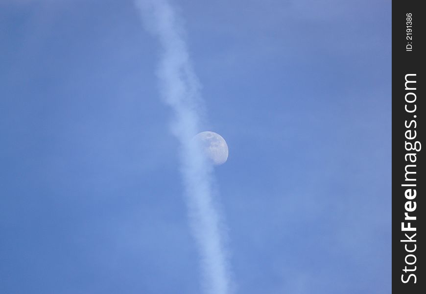 The moon half hidden behind an airplane trail, early evening. The moon half hidden behind an airplane trail, early evening