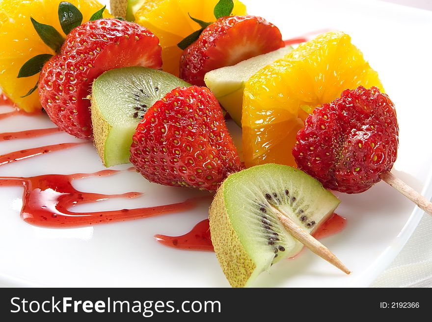 Fruit allsorts on skewers served atop of a plate decorated by strawberry jam