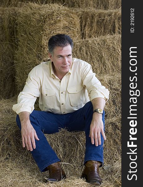 Handsome mature man sitting on some bales of hay at the end of an afternoon of working with the horses. Handsome mature man sitting on some bales of hay at the end of an afternoon of working with the horses.