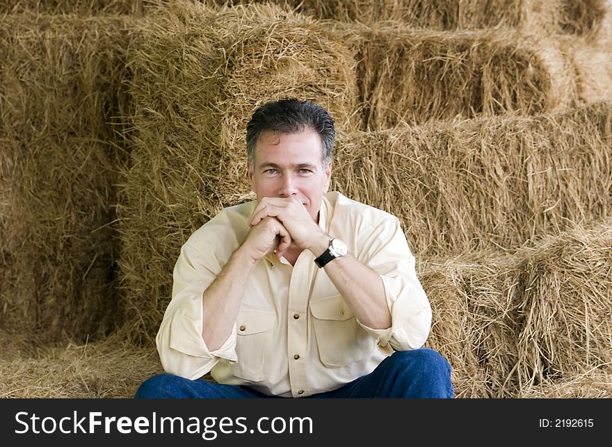 Handsome mature white male with a very contented, confident air about him sitting on stacks of fresh baled hay. Handsome mature white male with a very contented, confident air about him sitting on stacks of fresh baled hay.