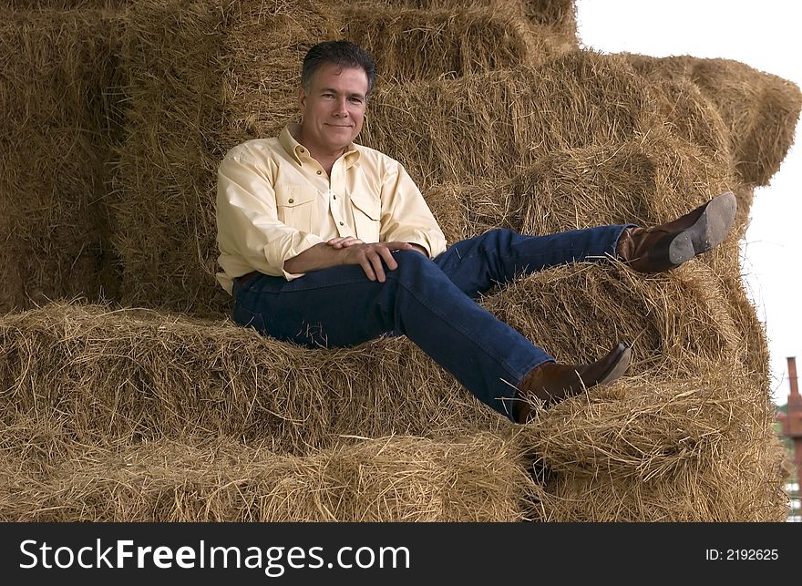 Handsome mature man sitting on a tall stack of bales of hay in the late afternoon. Handsome mature man sitting on a tall stack of bales of hay in the late afternoon.