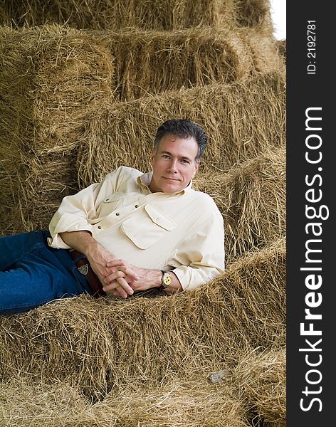 Handsome mature man lounging on a tall stack of bales of hay in the late afternoon. Handsome mature man lounging on a tall stack of bales of hay in the late afternoon.