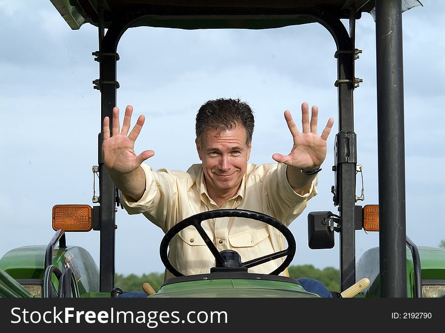 Man with a slightly worried smile sitting on a tractor gesturing with both hands in the air for something or someone to stop. Man with a slightly worried smile sitting on a tractor gesturing with both hands in the air for something or someone to stop.