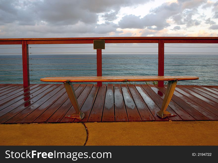 The bench is a sufboard overlooking the ocean on a boardwalk. The bench is a sufboard overlooking the ocean on a boardwalk