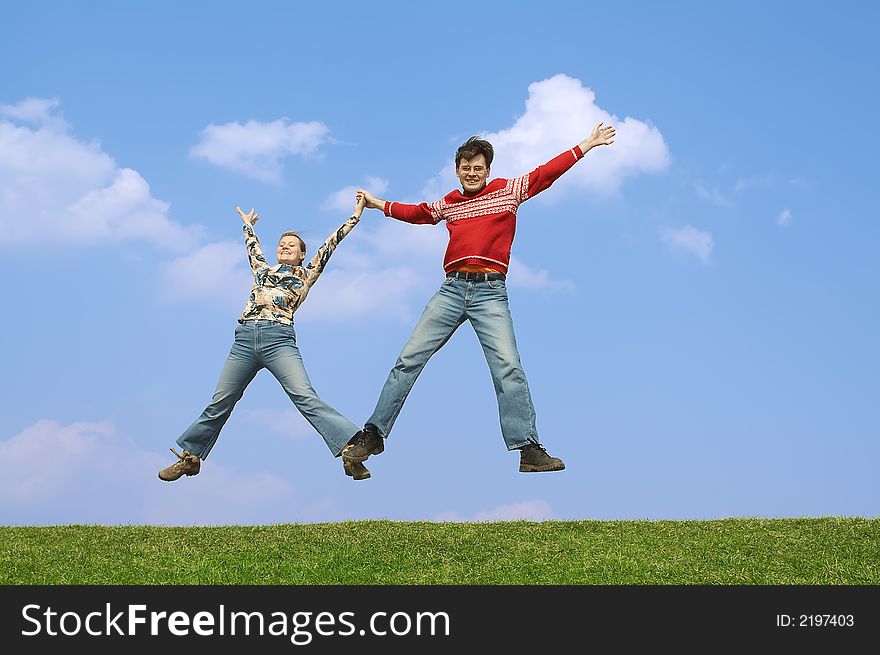 Two young people jumping on a green grass on a background of the dark blue sky with clouds. Two young people jumping on a green grass on a background of the dark blue sky with clouds