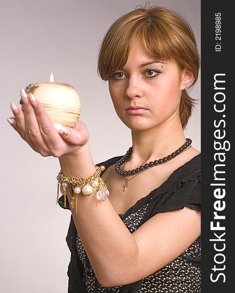 The girl looks at a candle in a hand on a grey background. The girl looks at a candle in a hand on a grey background