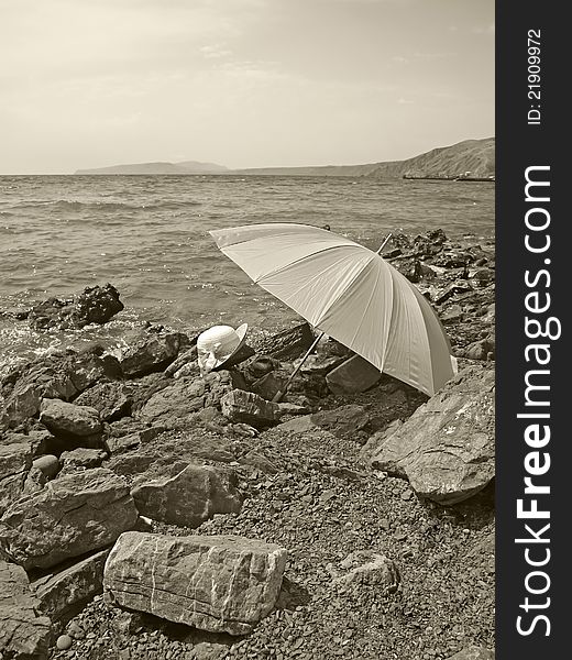 Summer hat and umbrella on a stony beach. Sepia image