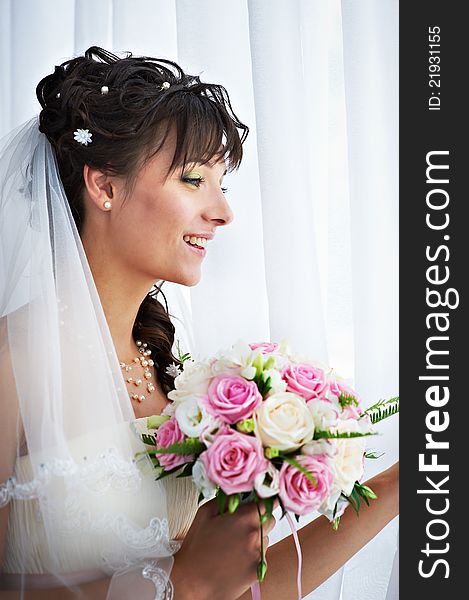 Happy bride with weding bouquet near window