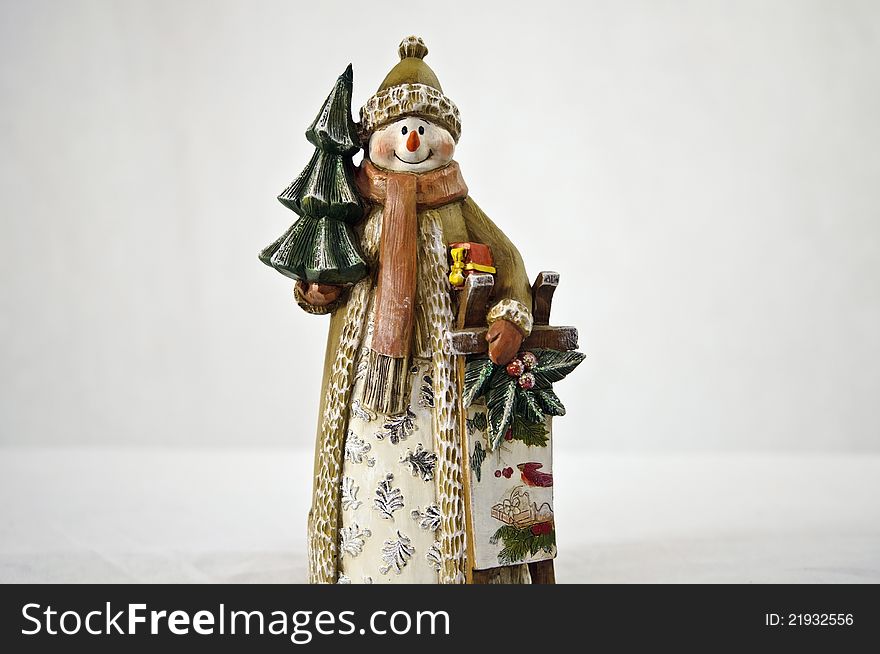 Snowman figure holding tree and sleigh on white