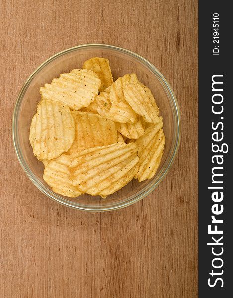 Rippled potato chips in the glass bowl over wooden background