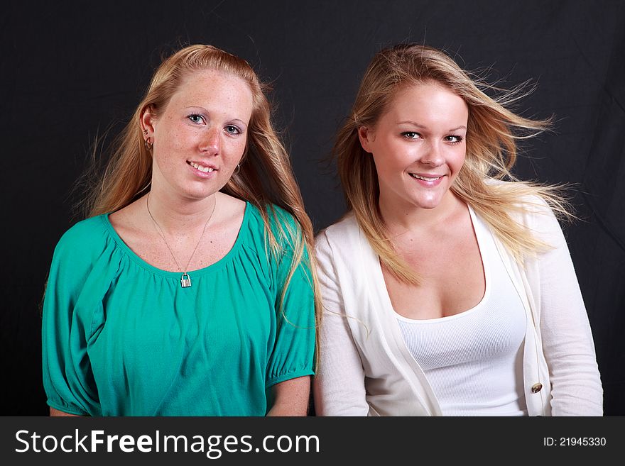 Two young adult girls with their hair blown looking happy on a black background