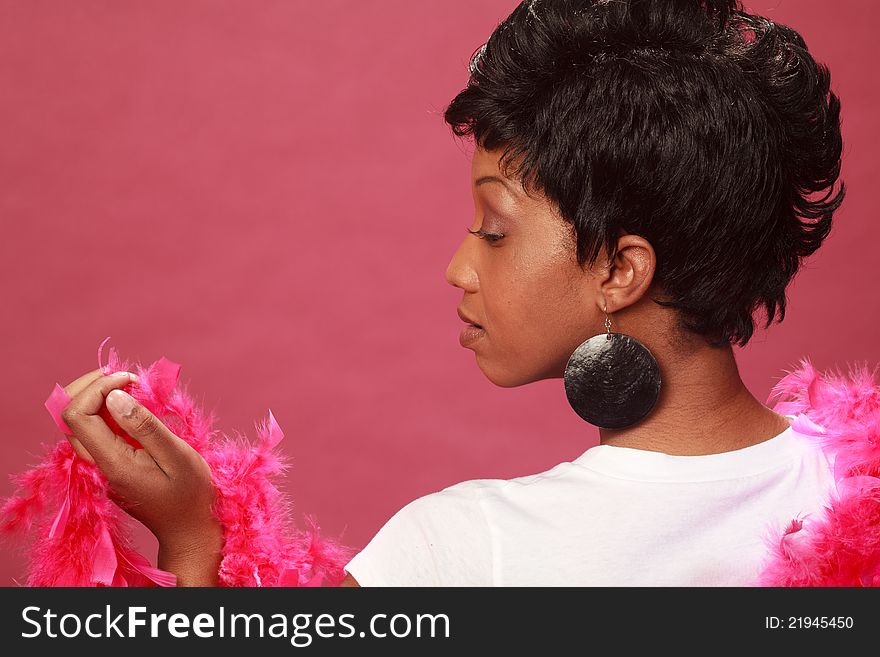 Beautiful black woman wearing a white shirt against a simple pink background with a feather boa.