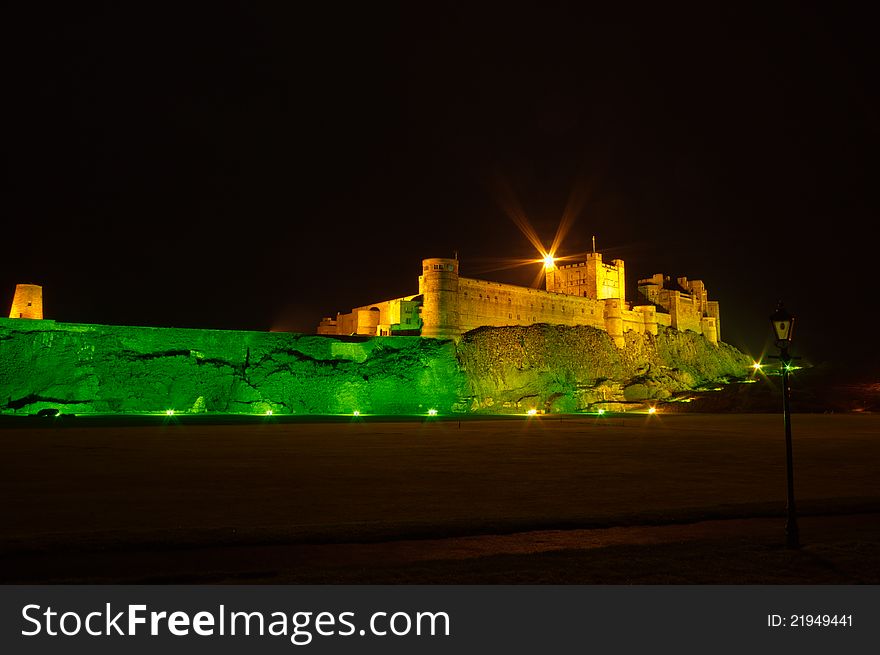 Bamburgh Castle at night illuminated by green and golden lights. Bamburgh Castle at night illuminated by green and golden lights