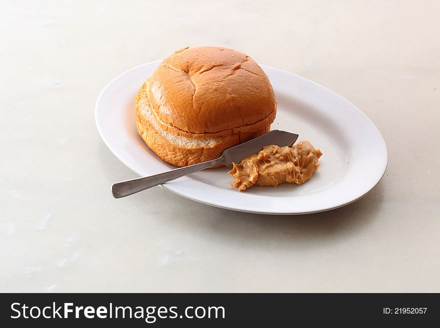 Bun on a white plate with peanut butter spread. Bun on a white plate with peanut butter spread