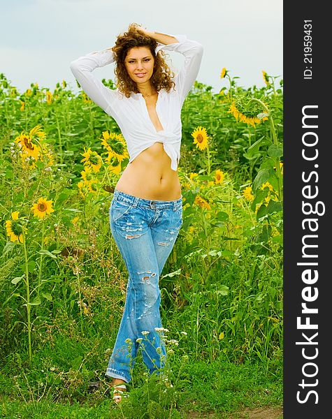 The girl in jeans and a white shirt costs in sunflowers. The girl in jeans and a white shirt costs in sunflowers