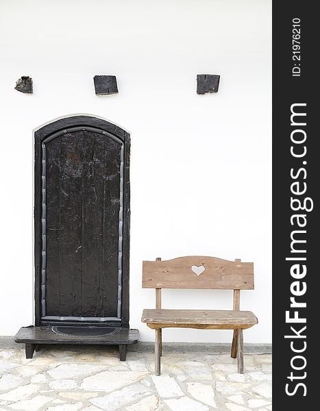 Detail of old Serbian house, wooden banch and black wooden doors against white wall. Detail of old Serbian house, wooden banch and black wooden doors against white wall