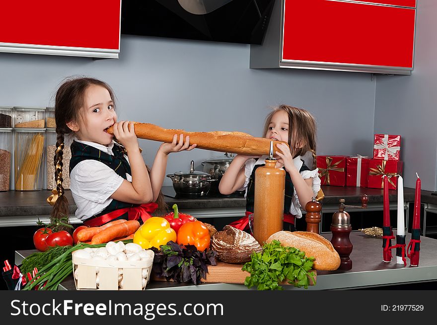 Two little girl in the kitchen of chef uniforms baguette bread bites against the kitchen table with fresh produce