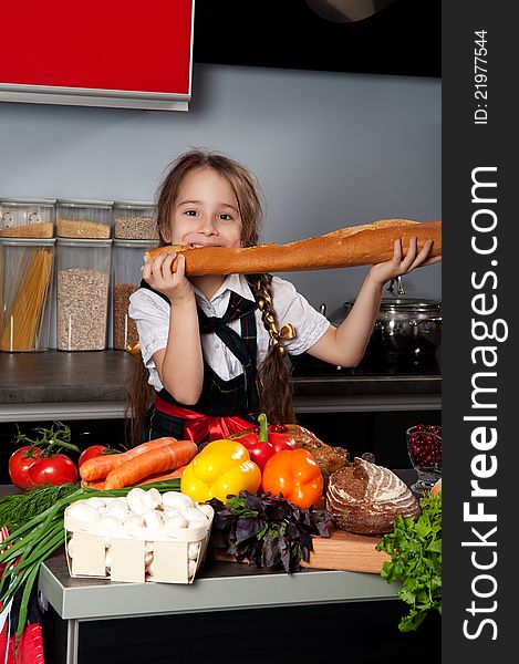The little girl in the kitchen of chef uniforms baguette bread bites against the kitchen table with fresh produce
