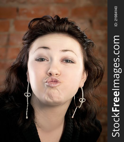 Pretty woman puckering lips into a kiss against brick background. Pretty woman puckering lips into a kiss against brick background