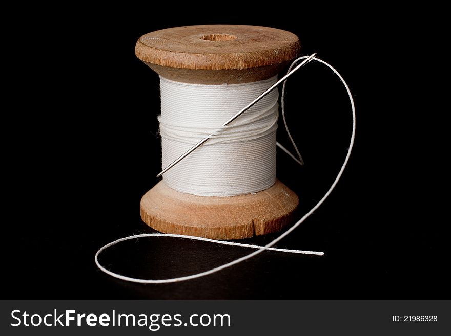 Spool of white thread and a needle over a black background. Spool of white thread and a needle over a black background