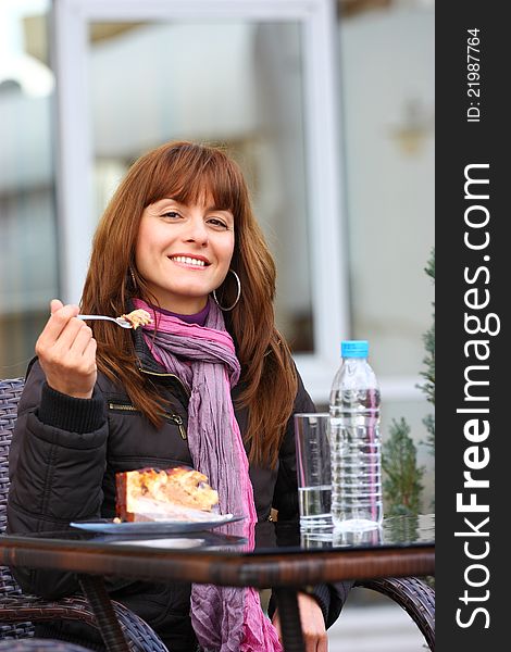 A happy woman enjoying her cake with a glass and bottle of water outdoor on her table. A happy woman enjoying her cake with a glass and bottle of water outdoor on her table