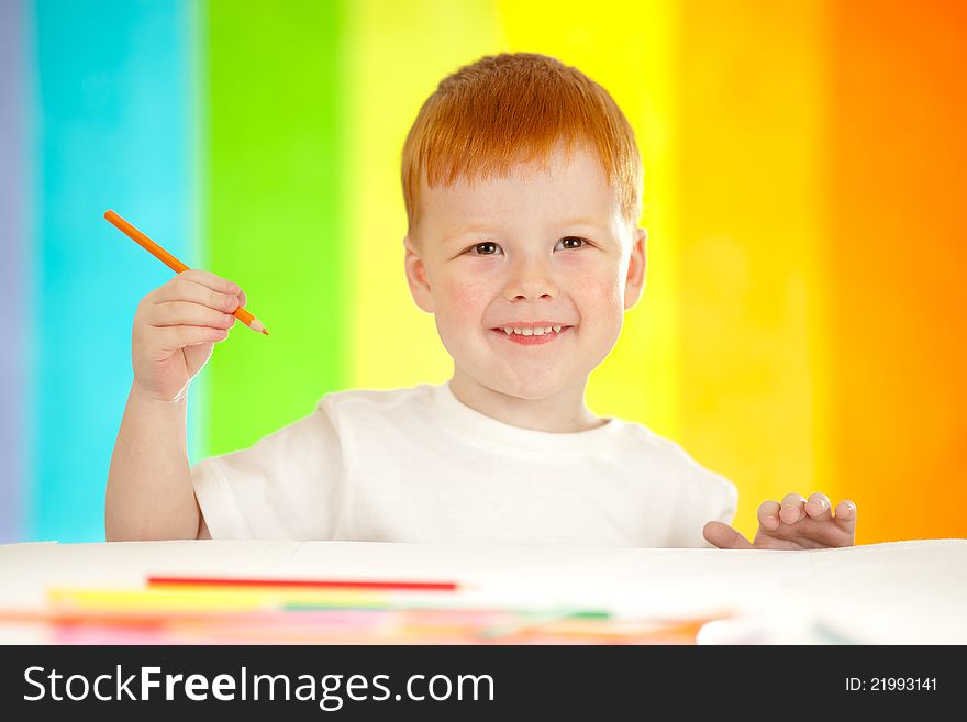 Red-haired adorable boy drawing with orange pencil on rainbow background. Red-haired adorable boy drawing with orange pencil on rainbow background