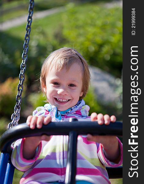 Portrait of smiling little girl on swing playground outdoors - looking at the camera. Portrait of smiling little girl on swing playground outdoors - looking at the camera