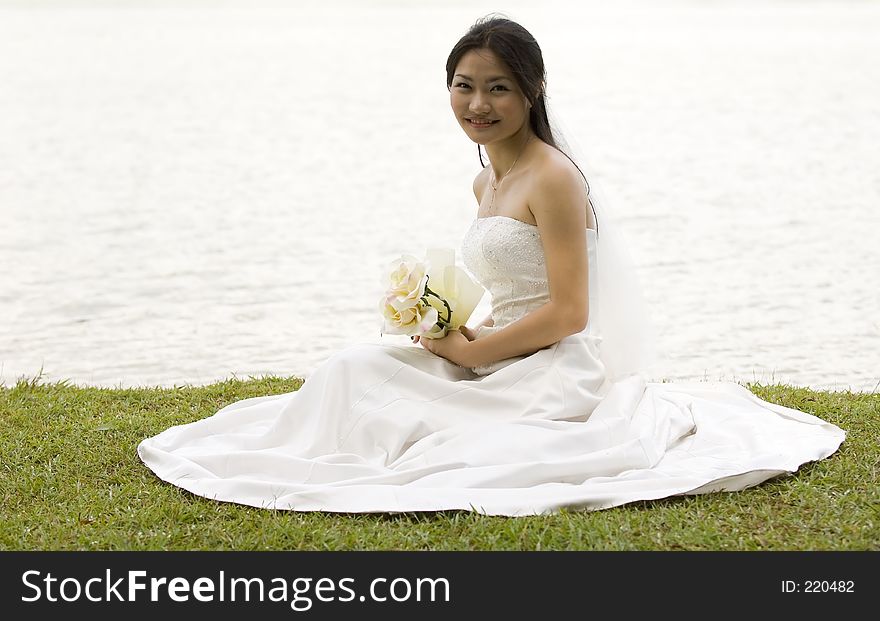 A beautiful young woman sits on a grassy bank in her wedding dress. A beautiful young woman sits on a grassy bank in her wedding dress