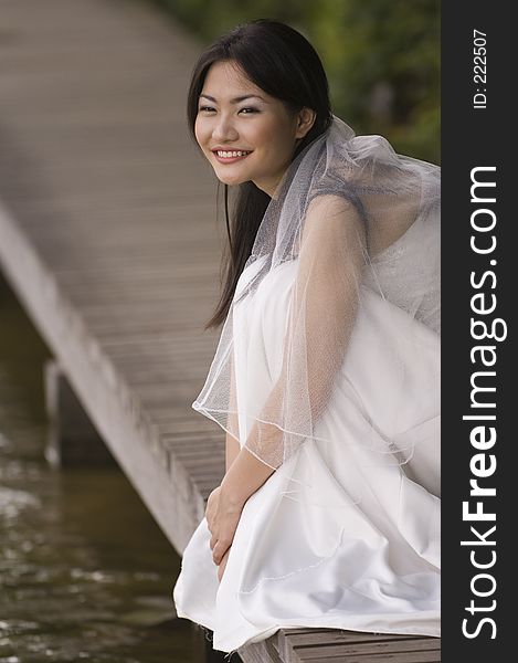 A beautiful asian bride sits on a boardwalk at the edge of a lake. A beautiful asian bride sits on a boardwalk at the edge of a lake