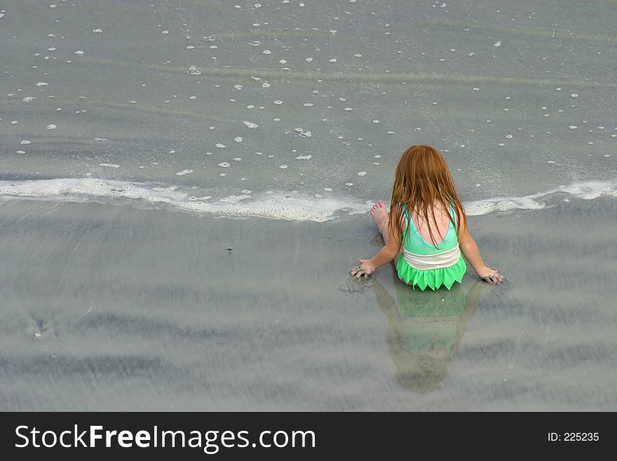 Little girl in green bathing suite on the beach, playing in the sand. Little girl in green bathing suite on the beach, playing in the sand.