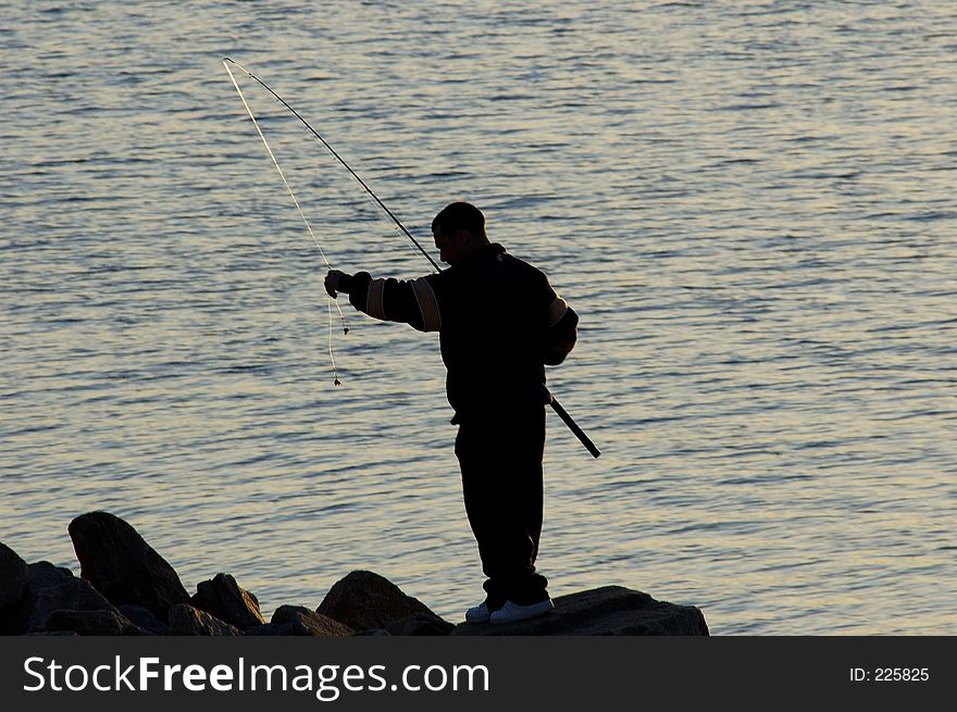 A silhouette of a man preparing to cast his fishing line as the sun goes down. A silhouette of a man preparing to cast his fishing line as the sun goes down.