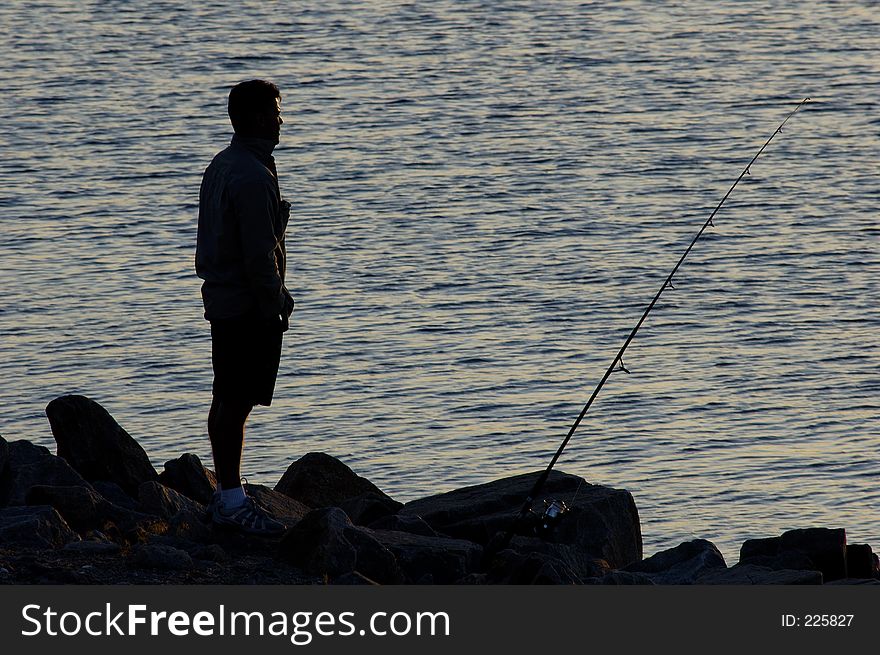 A silhouette of a man standing by his fishing pole as the sun goes down. A silhouette of a man standing by his fishing pole as the sun goes down