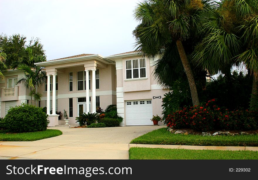 Beautiful home in tropics, with two sets of double columns and a wide driveway leading to front door, surrounded by tropical landscaping