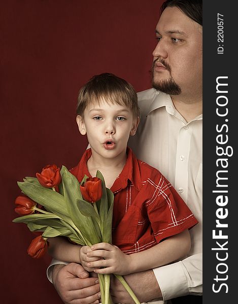 father and son in red shirt with red tulips on red background. father and son in red shirt with red tulips on red background