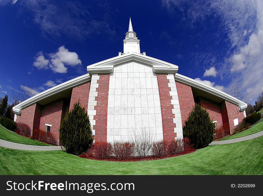 Wide angle shot of a brick church with green grass and blue sky