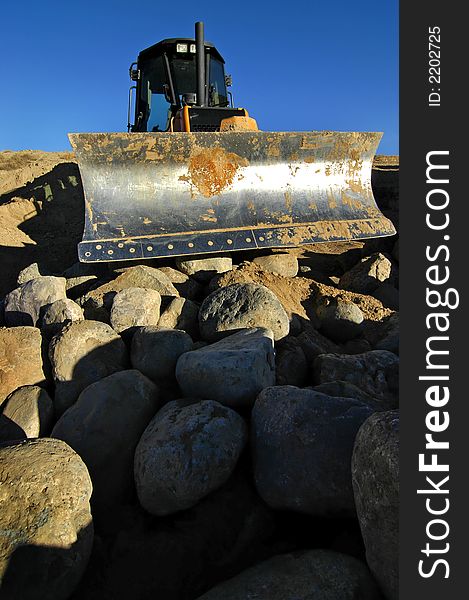 Bulldozer at construction site with boulders and blue sky