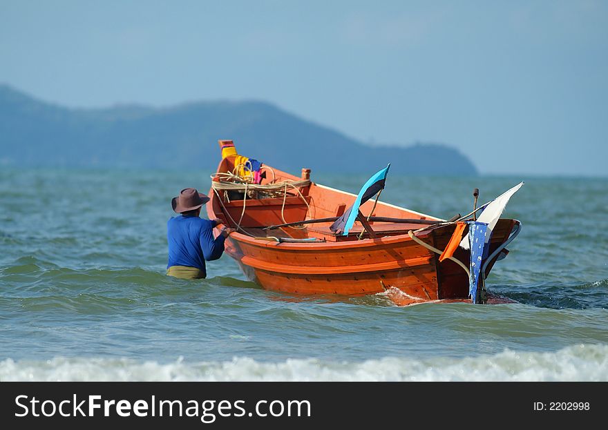 Fisherman in Rayong, Thailand taking his wooden boat out from the beach. Fisherman in Rayong, Thailand taking his wooden boat out from the beach