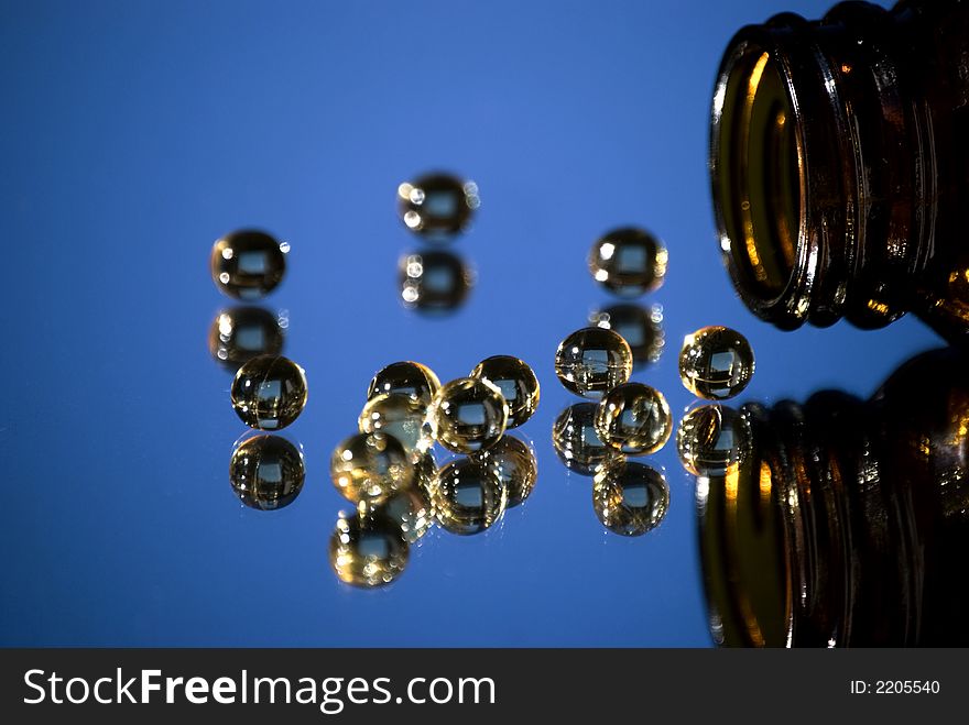 Clear pills spilling from bottle and reflection- blue background. Clear pills spilling from bottle and reflection- blue background